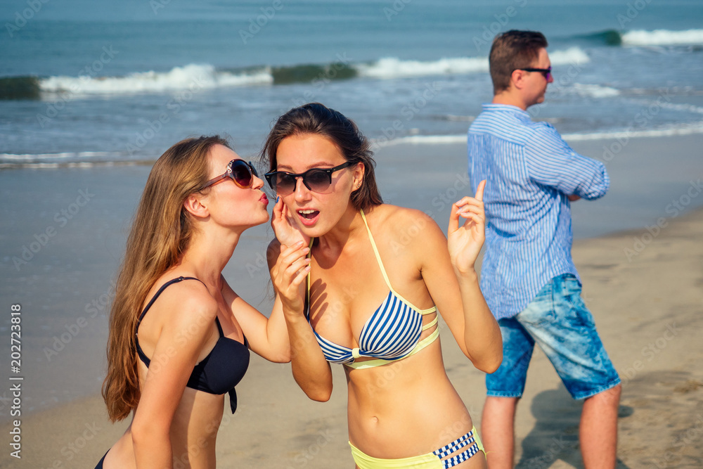 two beautiful and young women gossip about a man on the beach two beautiful and young women gossip about a man on the beach