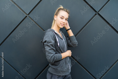 Portrait of young sports woman standing against a dark wall outdoors.