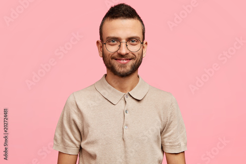Portrait of attractive young male student with stubble, rejoices successfull presentation of diploma paper, being clever, intelligent, poses against pink background. Positive human facial expressions © wayhome.studio 