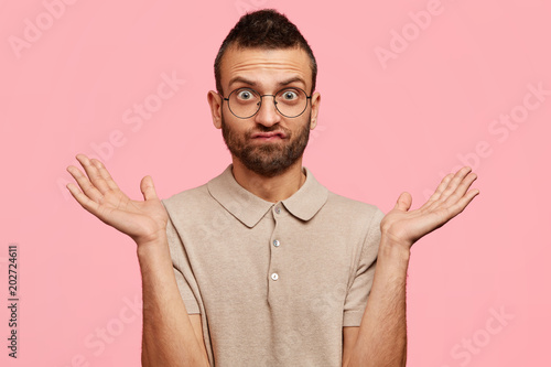 Принти на полотні Doubtful handsome unshaven male student shrugs shoulders with uncertainty, being