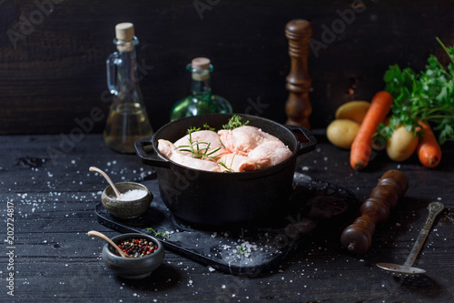 Raw chicken legs with solt andpepper in old clay dish on a black wooden rustic background. Copy space