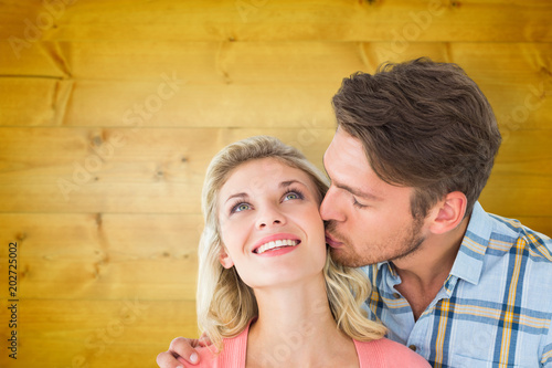 Handsome man kissing girlfriend on cheek against wooden planks background