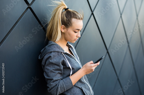 Fitness sporty woman lying on the black wall with smartphone in the city