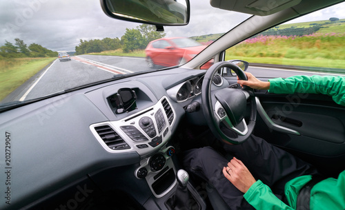 Obraz na płótnie The interior of a car of a female driver driving along a busy road in poor weather with traffic passing in the opposite direction on an English single carriageway. w salonie