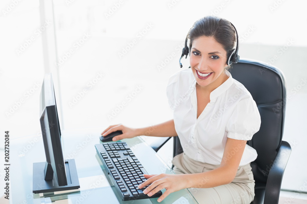 Happy call centre agent working on computer while on a call Happy call centre agent working on computer while on a call