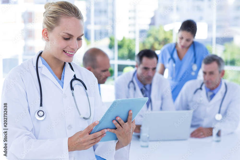 Smiling female doctor looking at clipboard while her colleagues works Smiling female doctor looking at clipboard while her colleagues works