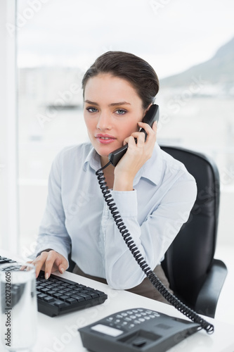 Businesswoman using landline phone at office desk