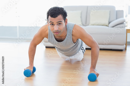 Sporty man with dumbbells doing push ups in the living room