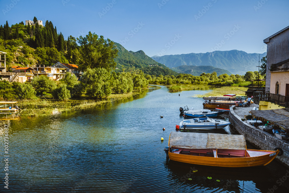 June, 8th, 2016 - Skadar Lake, Montenegro. Fishing boats, mountains and shore houses on Tsrnoyevicha river near Skadarsko Jezero in Montenegro. June, 8th, 2016 - Skadar Lake, Montenegro. Fishing boats, mountains and shore houses on Tsrnoyevicha river near Skadarsko Jezero in Montenegro.
