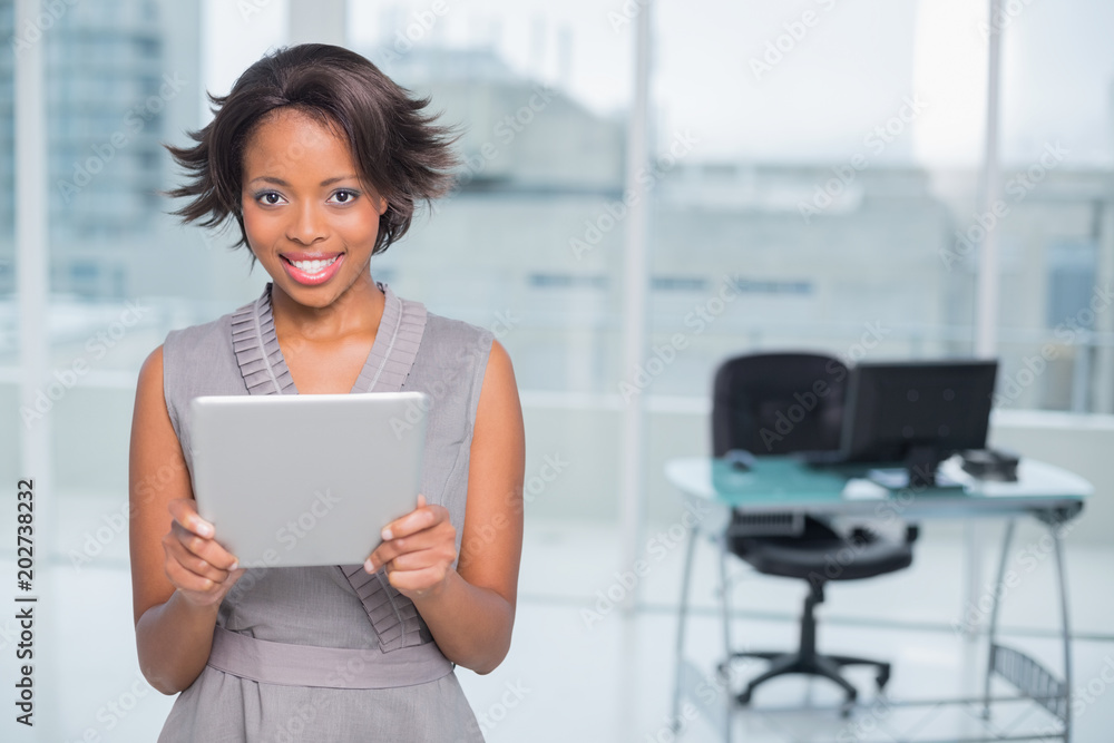 Smiling businesswoman standing in her office and holding tablet Smiling businesswoman standing in her office and holding tablet
