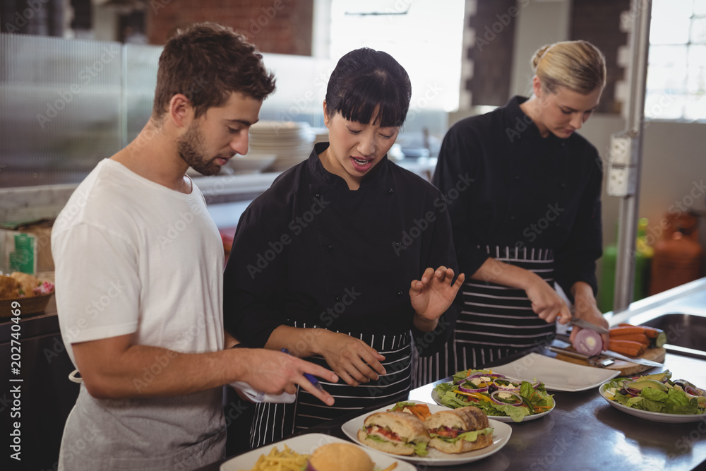 Female chef talking with waiter by colleague at kitchen Female chef talking with waiter by colleague at kitchen