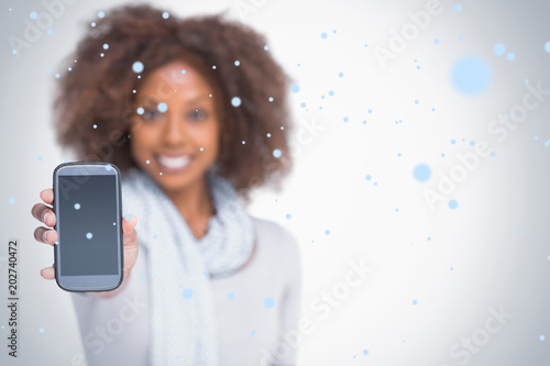 Woman with afro showing her smartphone against snow falling