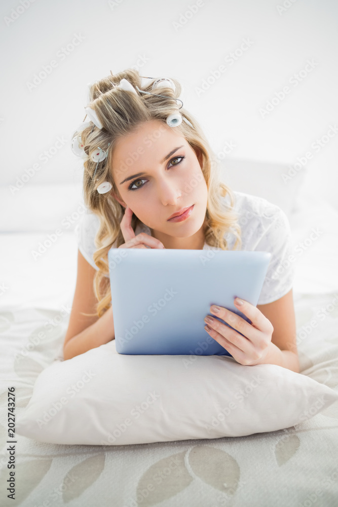Pensive pretty blonde wearing hair curlers using tablet pc Pensive pretty blonde wearing hair curlers using tablet pc