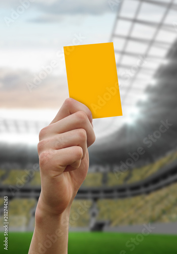 Hand holding up yellow card against football stadium
