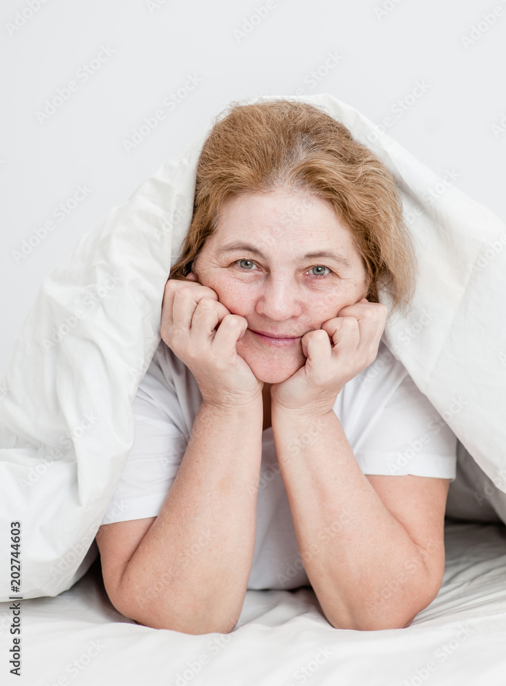 portrait of an elderly happy woman on a bed under a blanket portrait of an elderly happy woman on a bed under a blanket