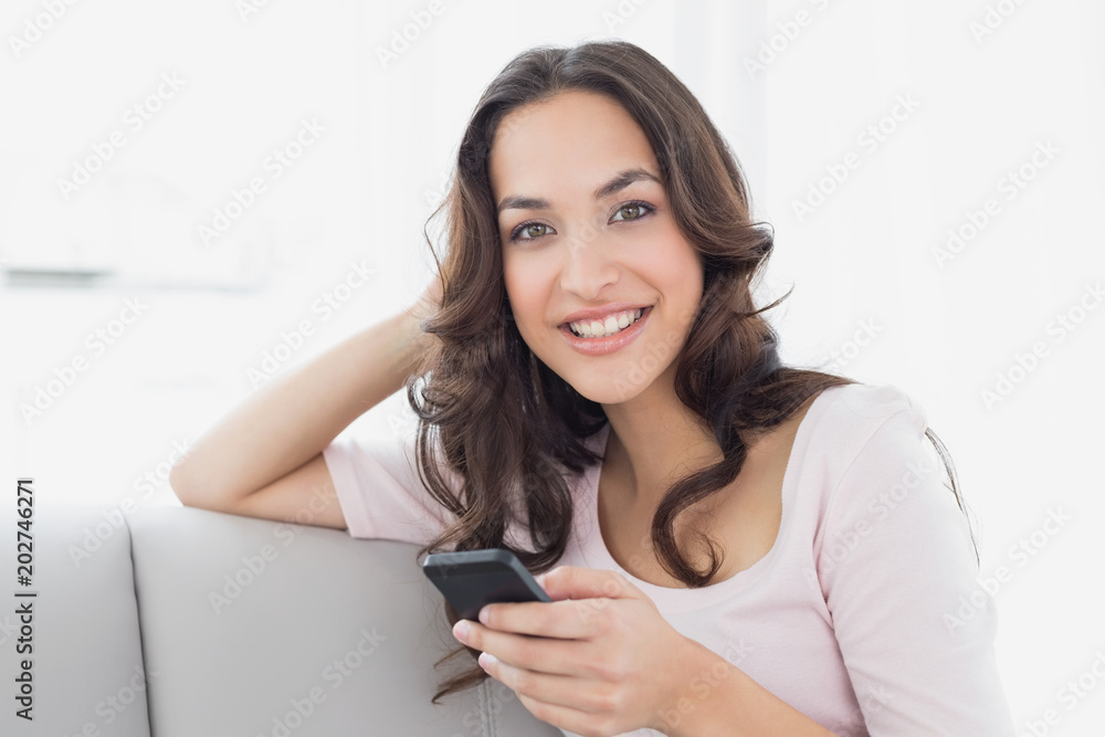 Smiling young woman text messaging on sofa at home Smiling young woman text messaging on sofa at home