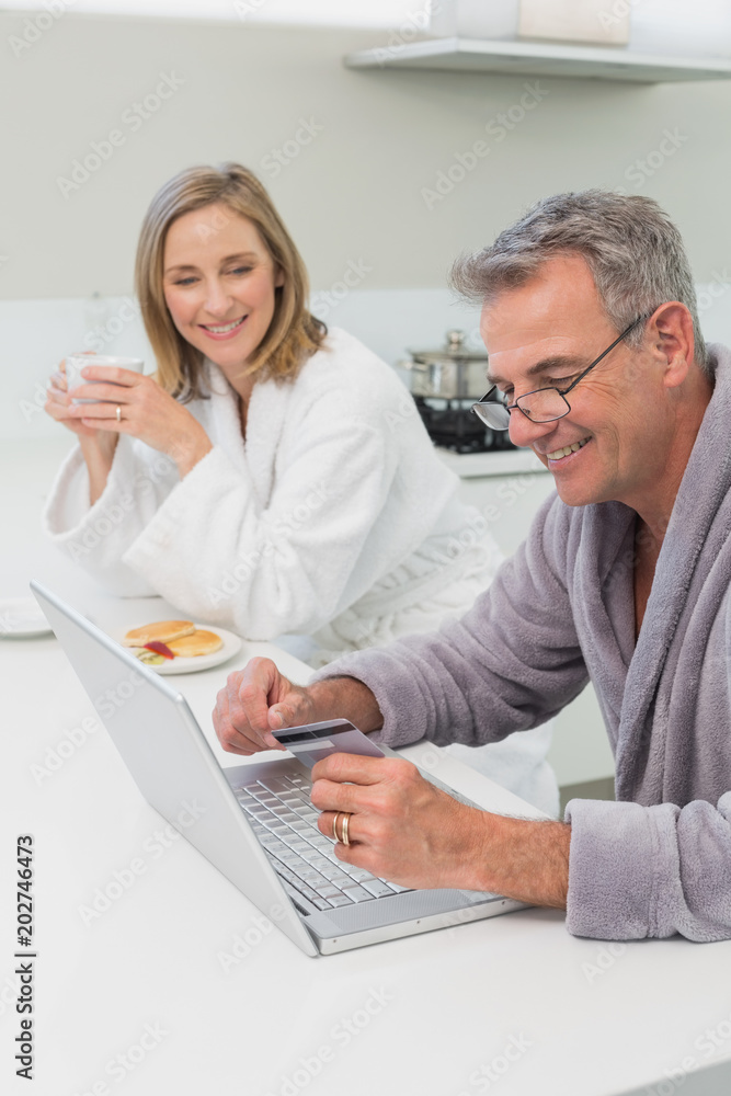 Happy couple in bathrobe doing online shopping at home Happy couple in bathrobe doing online shopping at home