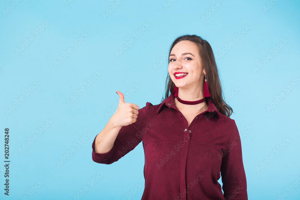 Cheerful young brunette caucasian student girl showing thumbs up on blue background with copy space Cheerful young brunette caucasian student girl showing thumbs up on blue background with copy space