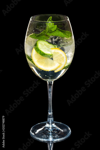 Cold Lemon and cucumber cocktail with a sparkling wine with ice cubes in wine glass isolated on black