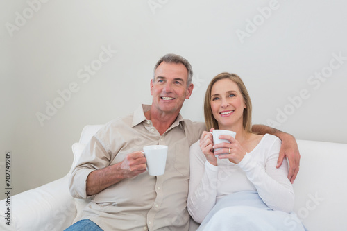 Loving couple with coffee cups looking away in living room