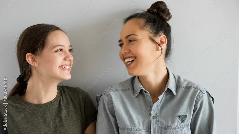 Two beautiful sisters embracing each other and smiling on gray background. Slow motion footage Two beautiful sisters embracing each other and smiling on gray background. Slow motion footage