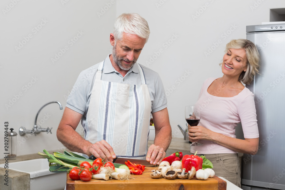 Man chopping vegetables while woman with wine glasses in kitchen Man chopping vegetables while woman with wine glasses in kitchen
