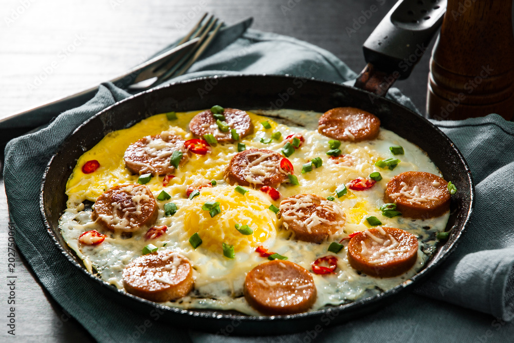 fried eggs with sausage and cheese in a frying pan on wooden table fried eggs with sausage and cheese in a frying pan on wooden table