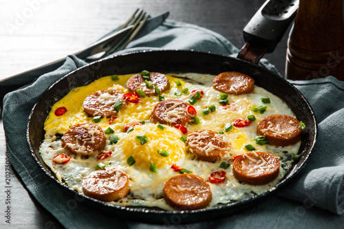 fried eggs with sausage and cheese in a frying pan on wooden table