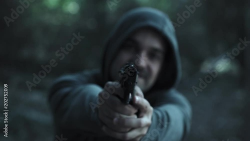 Crazy hooded young man pointing the gun at the camera