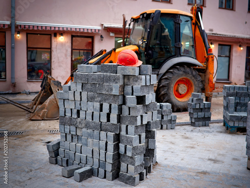 Pavement repair and laying of paving slabs on walkway, stacked tile cubes on the background. Stack of concrete blocks, sidewalk construction. Excavator on background.  photo