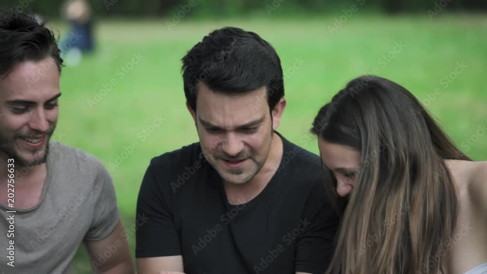 Friends Looking At smartphone. Young Friends Smiling in the park Friends Looking At smartphone. Young Friends Smiling in the park