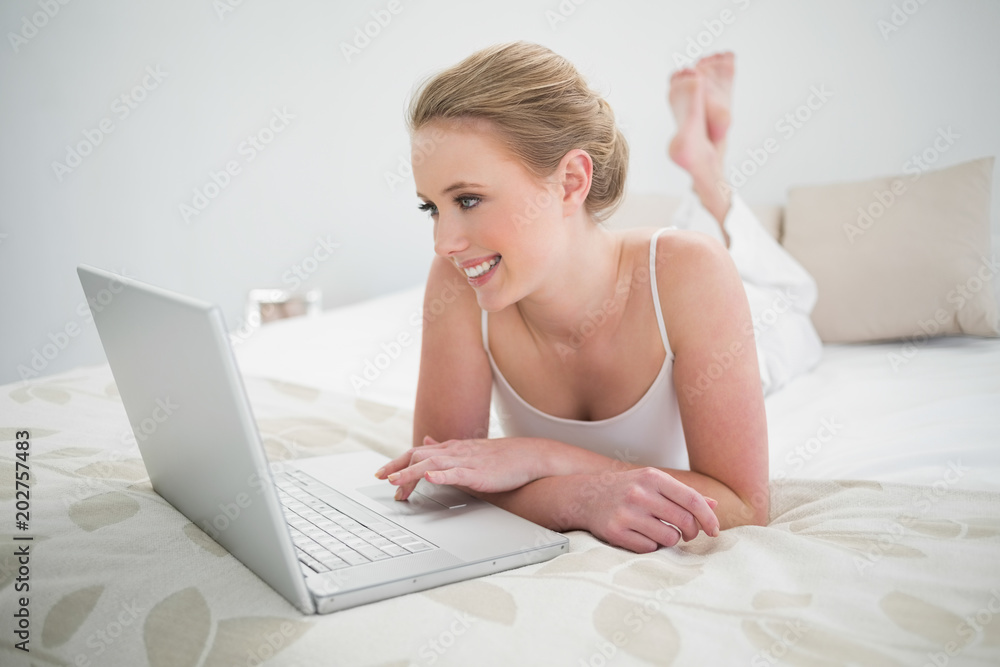 Natural smiling blonde using laptop and lying on bed Natural smiling blonde using laptop and lying on bed