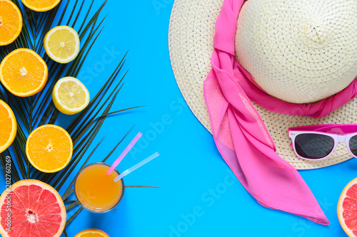 Beach hat, glasses, colorful citrus fruits sliced with palm leaf and juice over blue background