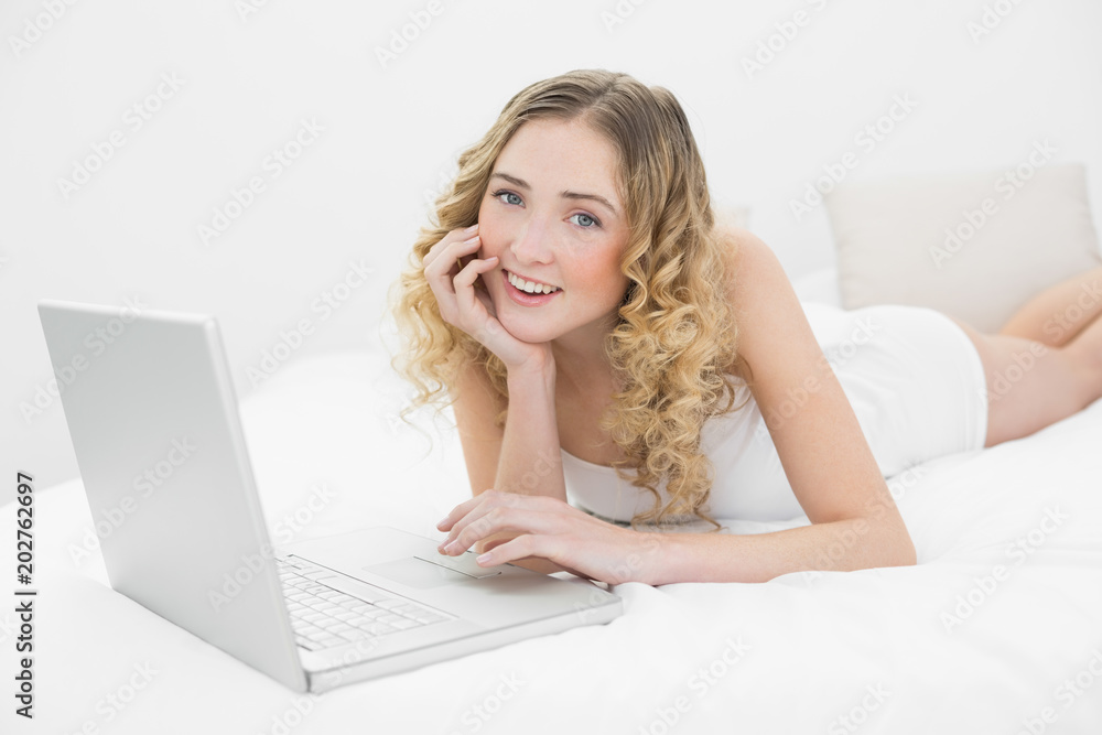 Pretty smiling blonde lying on bed using laptop Pretty smiling blonde lying on bed using laptop