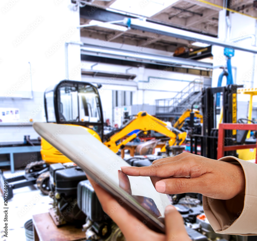 Female hands holding tablet pc against mechanic workshop Female hands holding tablet pc against mechanic workshop