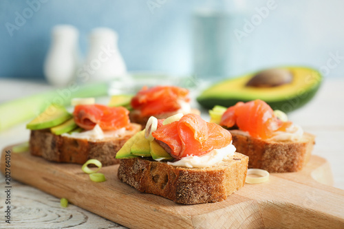 Tasty sandwiches with fresh sliced salmon fillet and avocado on wooden board, closeup
