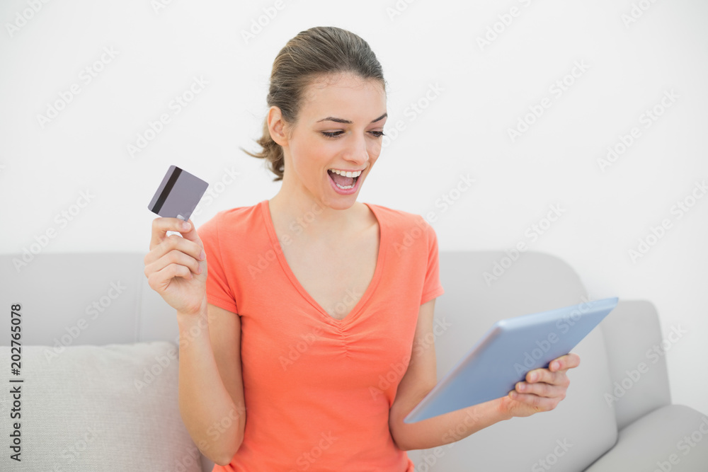 Cheerful casual woman home shopping with her tablet sitting on couch Cheerful casual woman home shopping with her tablet sitting on couch
