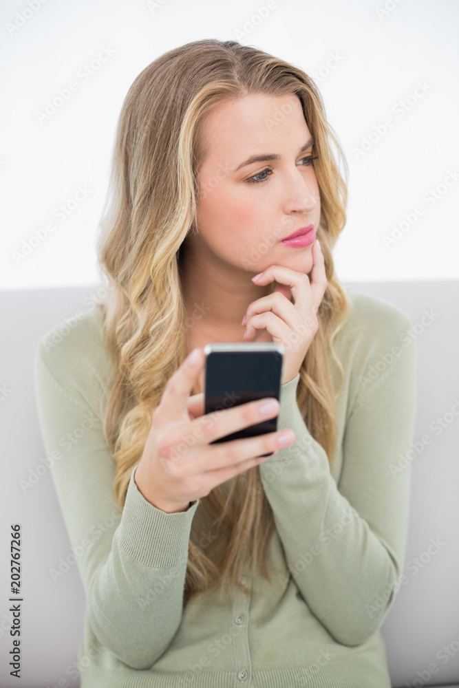 Pensive pretty blonde sending a text sitting on cosy sofa Pensive pretty blonde sending a text sitting on cosy sofa