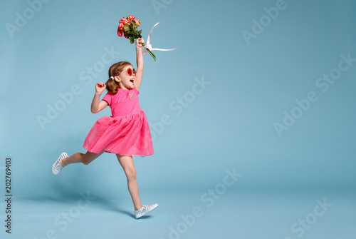 funny child girl runs and jumps with bouquet of flowers on colored background