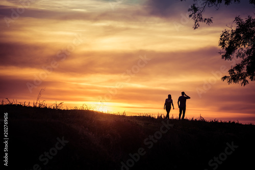 A couple of man and woman is walking and looking at amazing and beautiful sunset  with tree on one side  silhouette