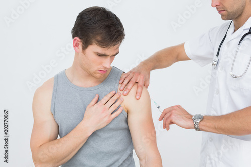 Male doctor injecting a young male patients arm