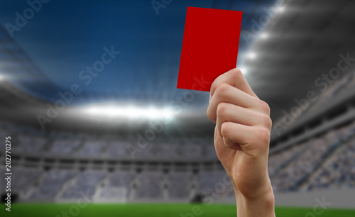 Hand holding up red card against football stadium
