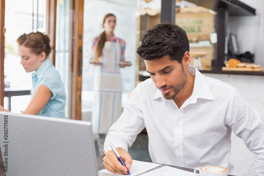 Man writing notes with laptop in coffee shop Man writing notes with laptop in coffee shop