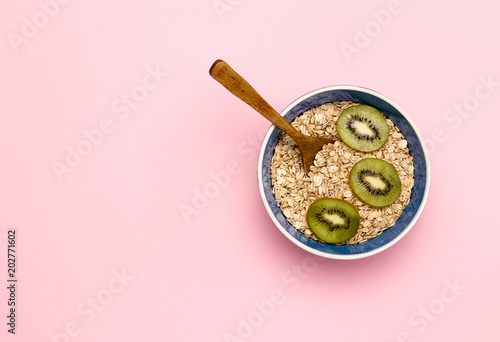 A bowl of oatmeal with kiwi on a pink background.