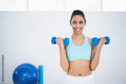 Sporty smiling woman lifting blue dumbbells