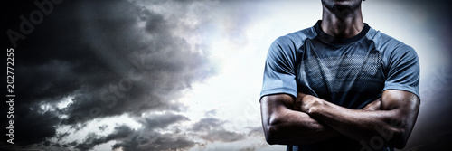 Canvas Print Thoughtful athlete standing with arms crossed against spotlight in sky