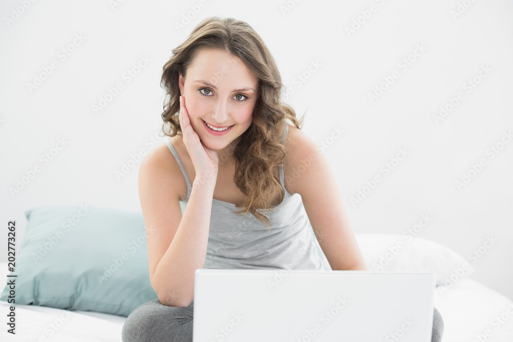 Smiling casual brunette with laptop sitting in bed Smiling casual brunette with laptop sitting in bed