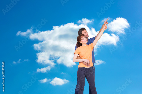 Happy couple pointing upwards together against cloudy sky