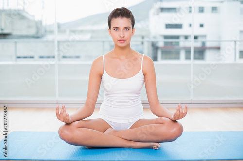 Calm natural brown haired woman in white sportswear practicing yoga