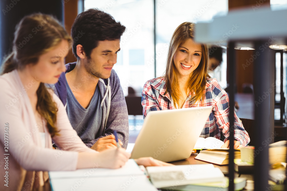 Student looking at camera while studying with classmates Student looking at camera while studying with classmates